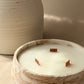 A close-up of a marble-look candle bowl with three wicks and the brand name 'BIUKA' in gold lettering, set against a warm beige background with a ceramic vase partially visible.